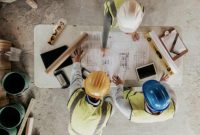 Ilustrasi pekerja konstruksi sedang memeriksa denah pembangunan rumah.
