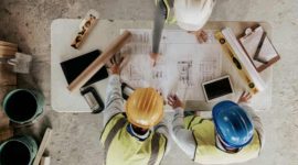 Ilustrasi pekerja konstruksi sedang memeriksa denah pembangunan rumah.
