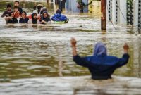 Sejumlah warga melintasi jalan permukiman yang terendam banjir tinggi saat proses evakuasi.
