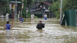 Sejumlah warga menyeberangi jalan yang terendam banjir tinggi saat hujan lebat melanda kawasan permukiman.