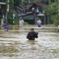 Sejumlah warga menyeberangi jalan yang terendam banjir tinggi saat hujan lebat melanda kawasan permukiman.