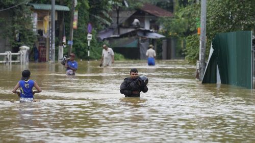 Sejumlah warga menyeberangi jalan yang terendam banjir tinggi saat hujan lebat melanda kawasan permukiman.