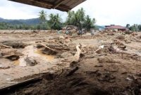 Kondisi permukiman yang porak-poranda setelah banjir bandang, dengan puing kayu dan lumpur menutupi area pemukiman.