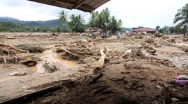 Kondisi permukiman yang porak-poranda setelah banjir bandang, dengan puing kayu dan lumpur menutupi area pemukiman.