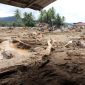 Kondisi permukiman yang porak-poranda setelah banjir bandang, dengan puing kayu dan lumpur menutupi area pemukiman.