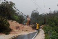 Seorang petugas memeriksa kondisi jalan yang tertutup longsor dan tiang listrik tumbang di tengah hujan deras pada jalur Tapanuli–Sibolga.