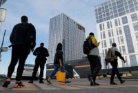 Pejalan kaki melewati kawasan gedung tinggi yang ditutup sementara dengan garis polisi.
