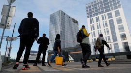 Pejalan kaki melewati kawasan gedung tinggi yang ditutup sementara dengan garis polisi.