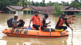 Petugas BNPB membawa seorang warga menggunakan perahu karet saat banjir merendam sejumlah rumah di sebuah kawasan permukiman.