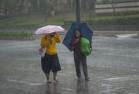 Dua warga berjalan di tengah hujan deras sambil menggunakan payung di salah satu ruas jalan Jakarta.