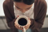 Seorang wanita memegang secangkir kopi hitam hangat.