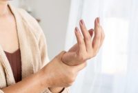 Seorang wanita menahan pergelangan tangannya, menunjukkan gejala nyeri atau pegal pada tangan.