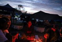 Orang-orang berkumpul di sekitar api unggun di dekat tenda-tenda pada malam hari di kawasan perkemahan, di tengah kondisi keamanan yang meningkat.