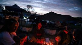 Orang-orang berkumpul di sekitar api unggun di dekat tenda-tenda pada malam hari di kawasan perkemahan, di tengah kondisi keamanan yang meningkat.