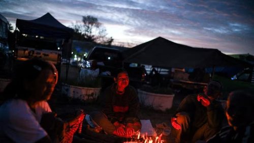 Orang-orang berkumpul di sekitar api unggun di dekat tenda-tenda pada malam hari di kawasan perkemahan, di tengah kondisi keamanan yang meningkat.