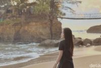 Seorang pengunjung menikmati pemandangan Pantai Sungai Suci, Bengkulu, dengan jembatan gantung kembar terlihat di belakangnya.