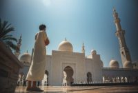 Seorang pria berdoa di halaman masjid megah dengan kubah putih dan menara tinggi di bawah langit cerah.