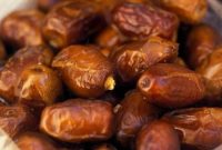 Kurma matang dengan tekstur keriput khas, berwarna cokelat hingga keemasan, tampak ditata dalam wadah.
