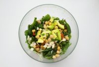 Semangkuk salad sehat berisi bayam segar, potongan alpukat, bawang, tomat, dan kacang chickpea yang kaya protein nabati.