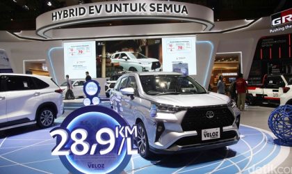 Orang melihat Toyota Veloz Hybrid di showroom dengan informasi pajak tahunan dan harga mobil terpajang di dekat kendaraan.