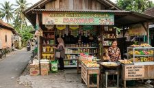 Seorang pedagang melayani pembeli di warung sembako sekaligus menjual gorengan di teras rumah