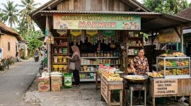 Seorang pedagang melayani pembeli di warung sembako sekaligus menjual gorengan di teras rumah