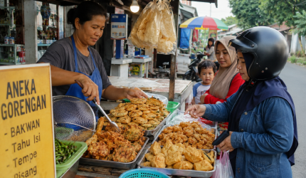 Ilustrasi pedagang gorengan pinggir jalan dengan berbagai jenis gorengan seperti bakwan, tahu isi, dan tempe mendoan yang tersaji di etalase sederhana di pinggir jalan kampung.